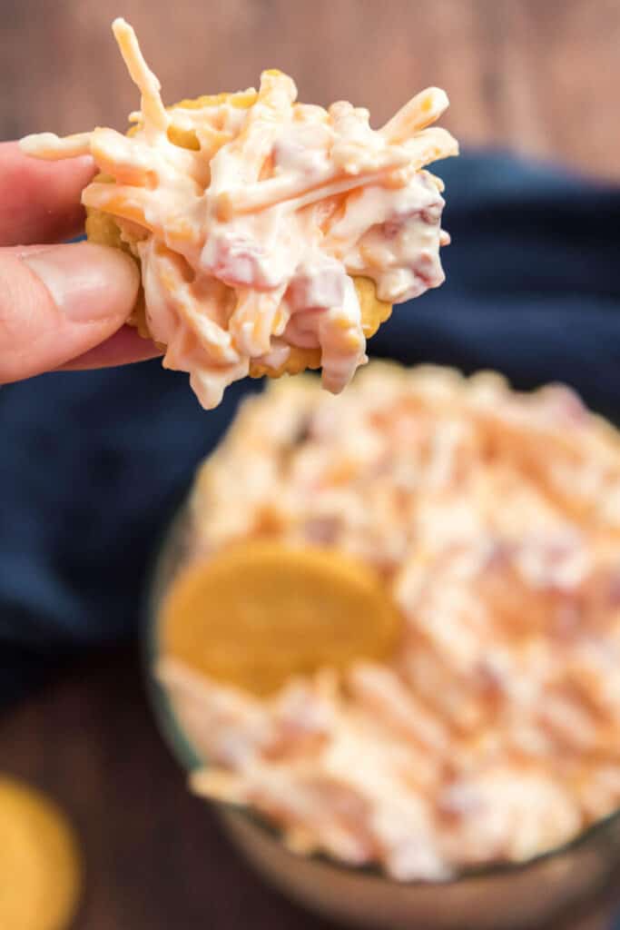 fingers holding pimento cheese dip on a cracker