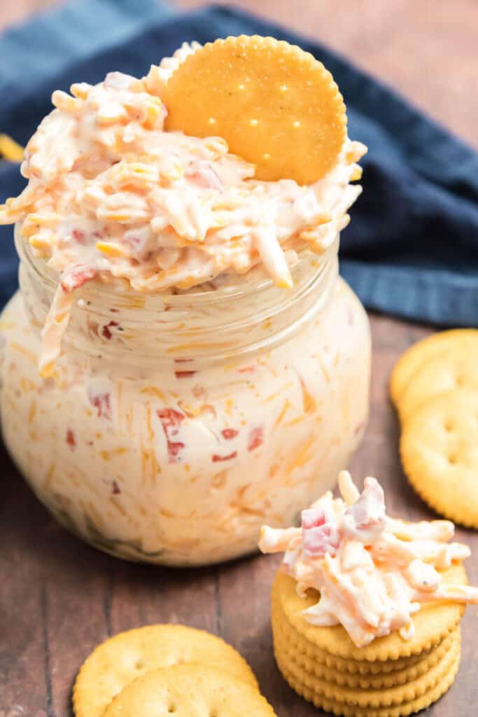 pimento cheese dip in a mason jar  with a ritz cracker sticking out of the top