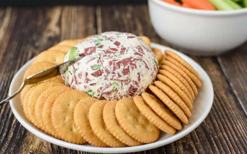 dried beef cheese ball on white plate and wooden table with ritz crackers