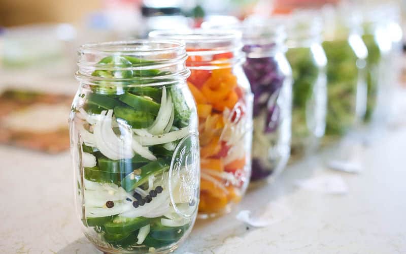 ball mason jars lined up with quick pickled jalapenos with onions and peppercorns in jar
