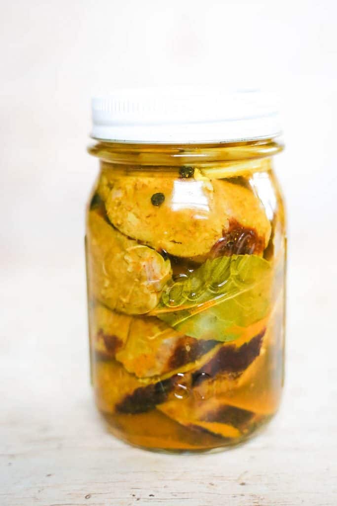 close up of pickled sausage with bay leaf and peppercorns in mason jar