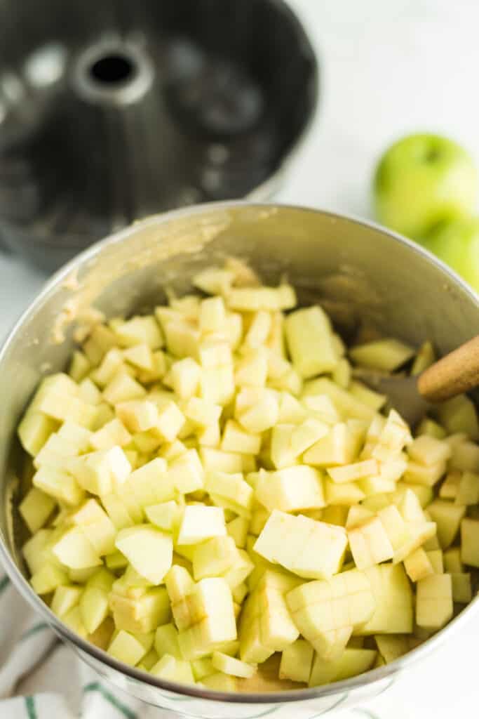 apples in a mixing bowl with a spoon for an apple pound cake with caramel frosting