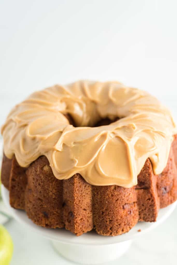 caramel icing on apple pound cake on white cake stand ready to eat for potluck