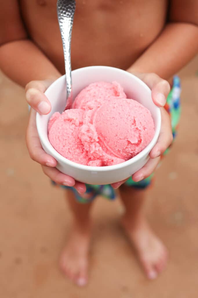 tan child holding white bowl of homemade ice cream 