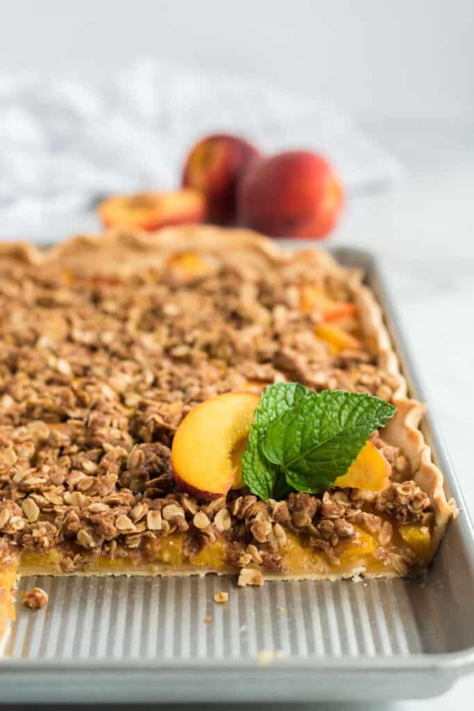 peach crumble slab pie in a jelly roll pan with peach on top