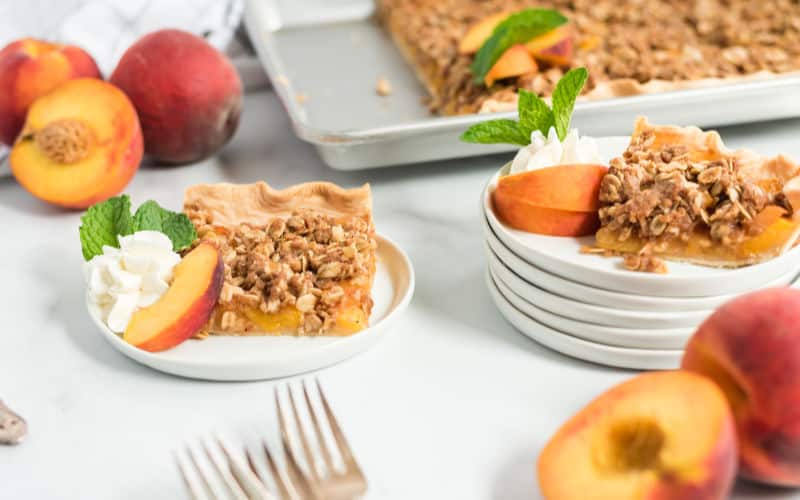 a peach crumble slab pie on a plate with peaches and cream