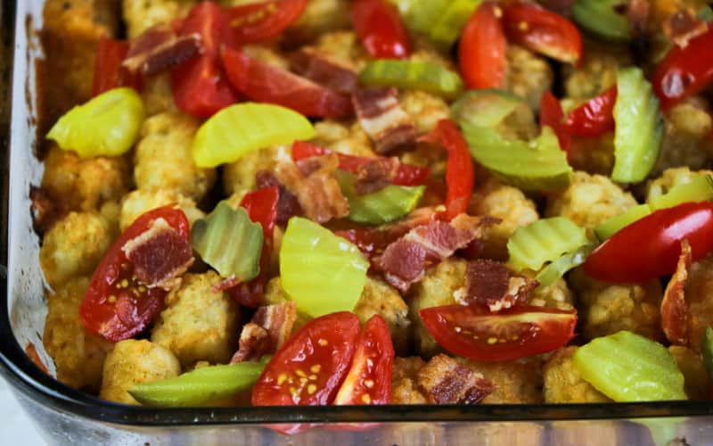 pickles and tomatoes on top of the bacon cheeseburger tater tot casserole
